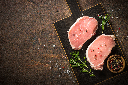 Fresh pork meat. Pork steaks on cutting board with ingredients for cooking. Top view at dark stone table with copy space.
