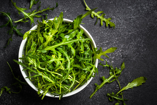 Arugula fresh green leaves in the bowl at black stone table.