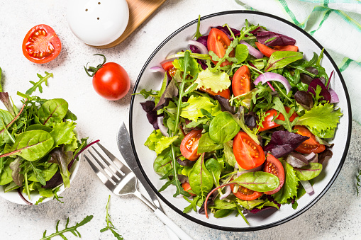 Green salad from fresh salad leaves and vegetables in white plate. Healthy vegan food. Top view image.