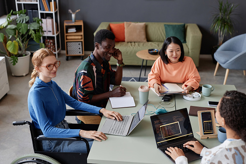 Portrait of young diverse IT team meeting at table in office and discussing project, copy space