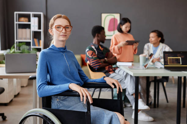 istock Young woman using wheelchair in office with team in background 1726237350