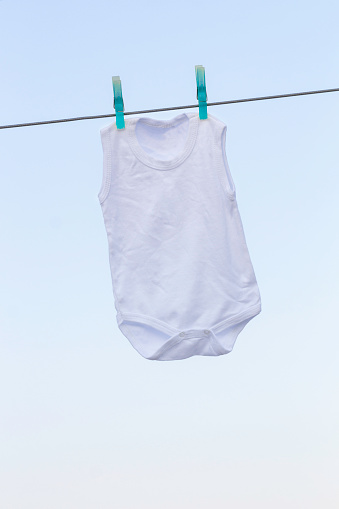White baby clothes on clothesline with clear sky in background.Laundry is drying on a rope outdoors under blue sky.