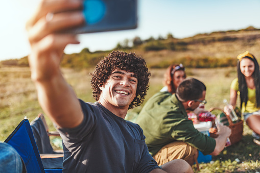 Happy young man enjoys a nice day in nature. He's smiling and taking selfie with smartphone.