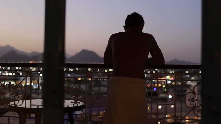 silhouette of a man in the evening on a balcony overlooking the city and mountains uses a smartphone.