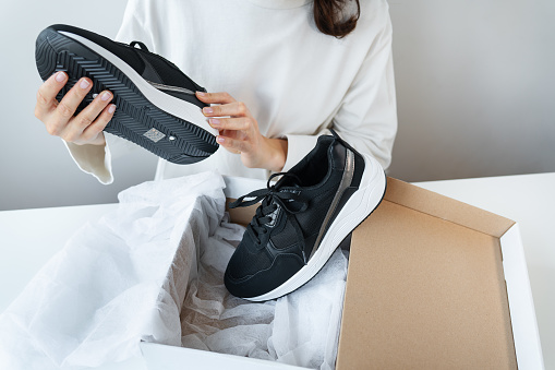 A young girl sits at a table and looks at her new sneakers from a box. Online shopping, payment by card, delivery by courier