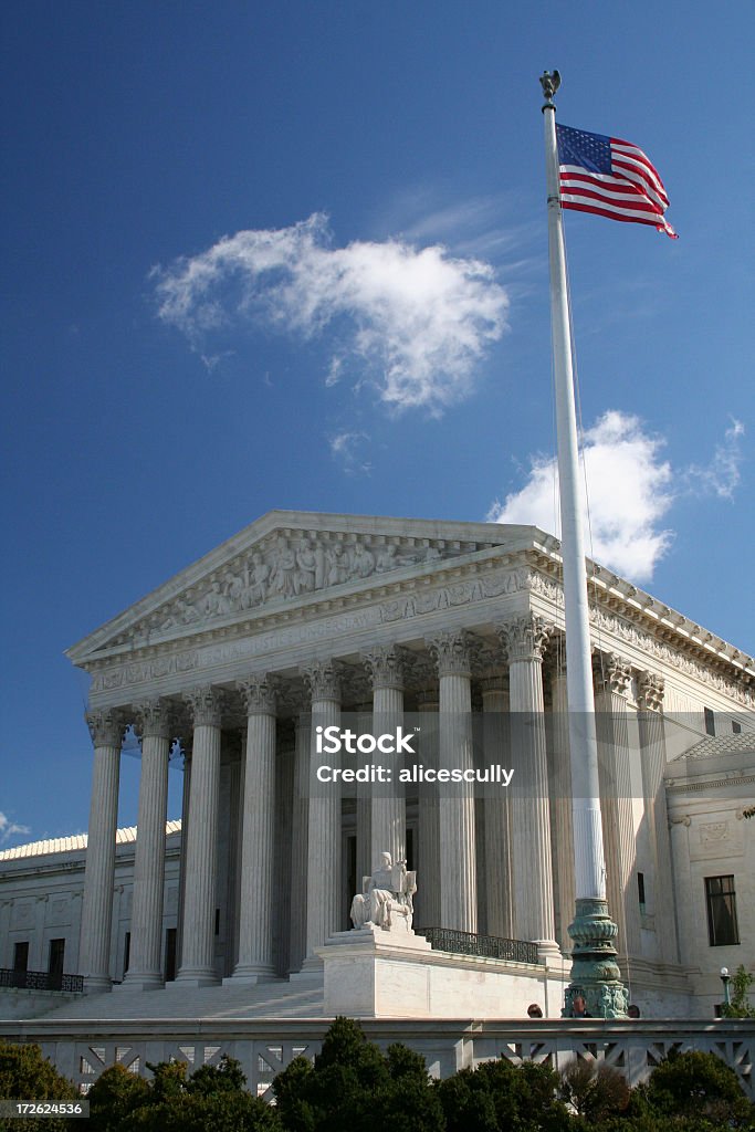 US Supreme Court Flag View US Supreme Court building with US flag against blue sky dotted with white clouds. American Flag Stock Photo