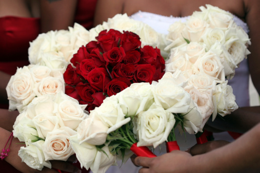 A bride displays her bouquet of red roses encircled by the white rose bouquets of her bridesmaids.