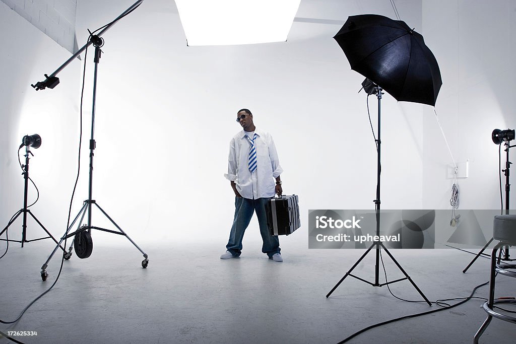 A man standing with a case in a white studio with lighting "Man stands in place, surrounded by studio lighting equipment." Order Stock Photo