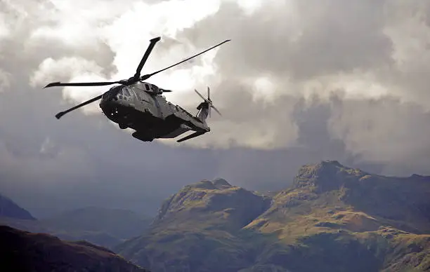 Low level RAF Merlin helicopter hugs valleys in the lake district mountains during poor weather exercise