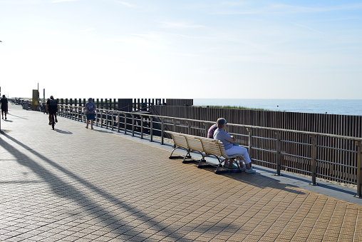 Ostend, West-Flanders, Belgium - October 1, 2023: elegant couple, white man and Asian woman walking on the boardwalk wearing sunglasses and the sun in their back