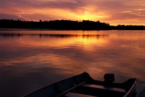 A beautiful sunset on a Muskoka lake with a fishing boat in the forground.