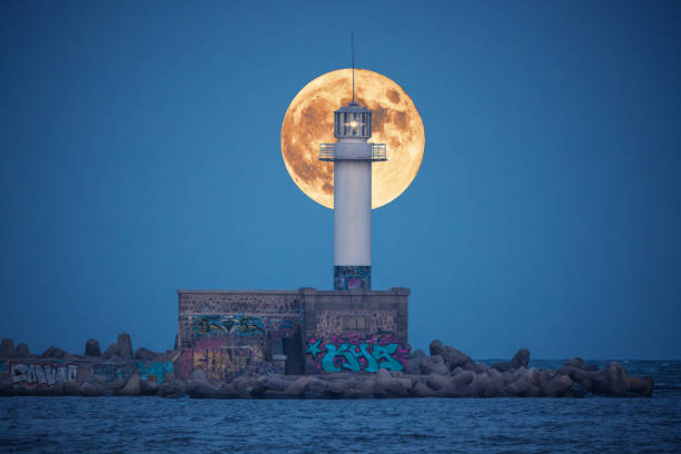 paisagem crepuscular da lua cheia sobre o horizonte do mar e iluminação do farol da costa - lighthouse beacon sailing storm - fotografias e filmes do acervo