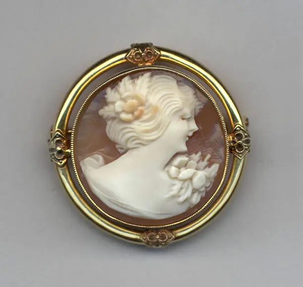 Antique Italian shell cameo of girl in gown with floral bouquet in decorative gold setting.