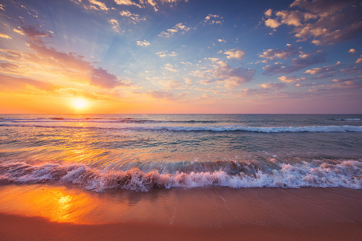 Beautiful cloudscape over ocean waves and tropical beach, sea horizon at sunrise.