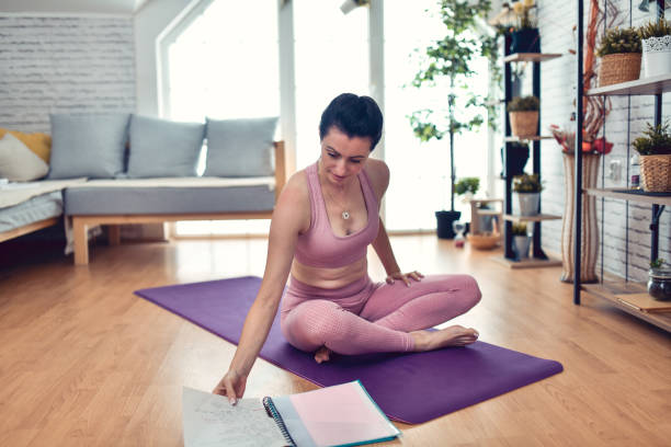 istock Yogini Sitting Cross Legged On Mat And Looking Through Her Workout Plan 1726290229