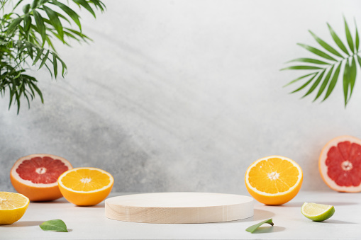 Empty wooden round podium on light grey background surrounded by citrus fruits