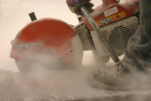 a detailed shot of a petrol cutter cutting a large kerb showing dust from sawcut