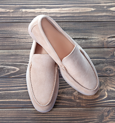 Pair of beige suede loafers on a wooden background