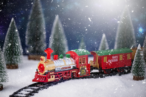 Toy train on railway in the snow with Christmas tree. Christmas and New Year background. Creative winter Christmas composition.
