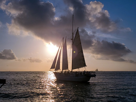 This is a photograph of a large sailboat sailing at sunset in the Gulf of Mexico on the coast of Key West, a Florida, USA travel destination on a winter day.
