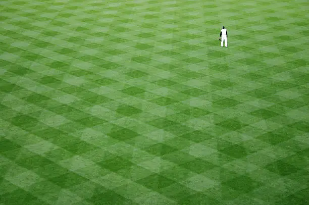 Baseball player awaits ball on perfectly manicured baseball stadium lawn.