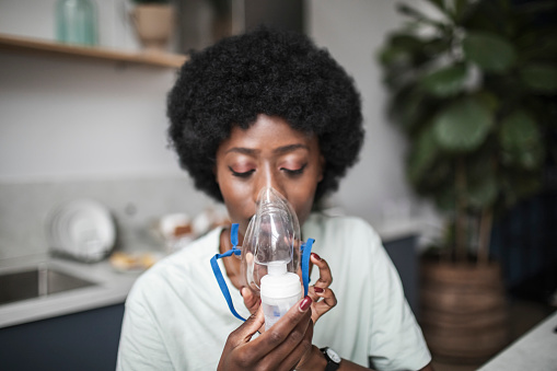 Young adult black woman suffering asthma using nebuliser at home