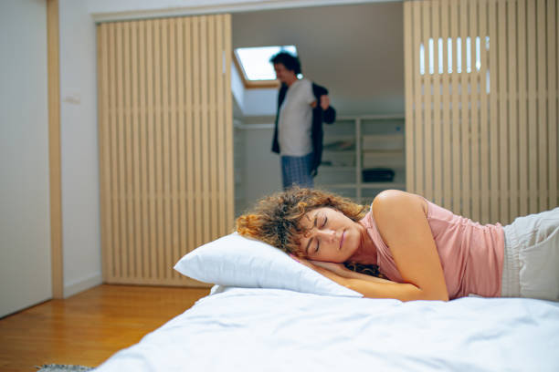 istock Woman is sleeping in bed while man is getting dressed in closet 1726400907