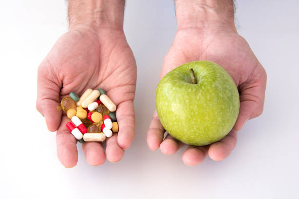 istock man's hand with one with a green apple and hand with pills 1726414582