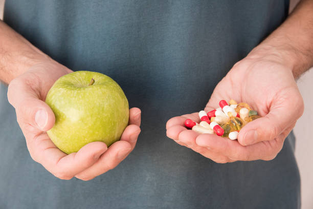 istock man's hand with one with a green apple and hand with pills 1726414585