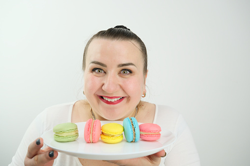 satisfied and happy woman eating macaroons on white background space for text advertising sweets goodies pleasant life pleasure buzz joy. smile overweight model size plus