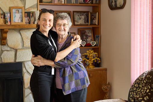 Portrait of a smiling young woman standing arm in arm with her senior grandmother during a family visit together