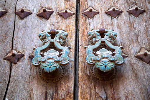Antique wooden door aged over time with two ornate greenish metallic knockers