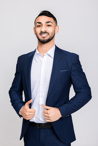 Serious concentrated young turkish buisnessman wearing fashionable suit and whiite modern shirt successful man standing over grey background in studio isolated.
