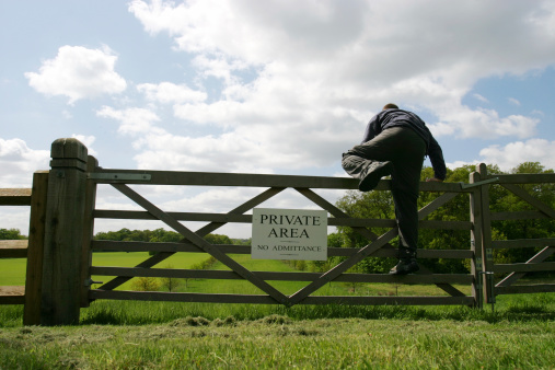 A man climbing over a gate into a 'Private area'