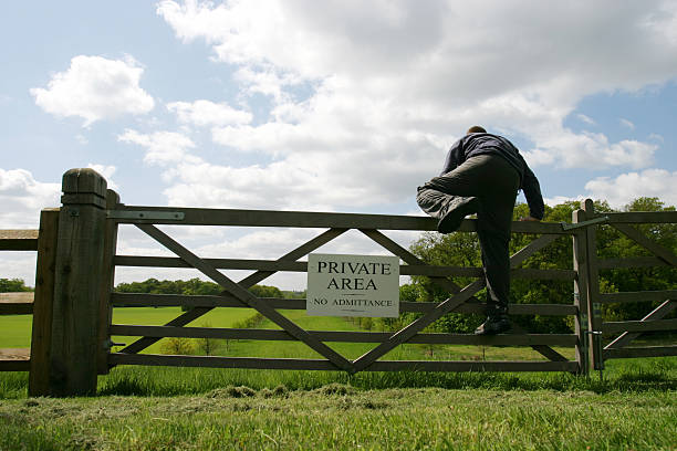 Breaking the rules A man climbing over a gate into a 'Private area' burglar fence stock pictures, royalty-free photos & images