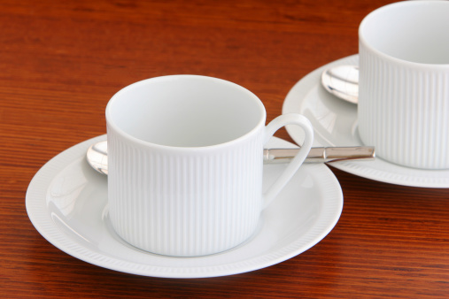 Two white tea or coffee cup and saucers on a wooden table.