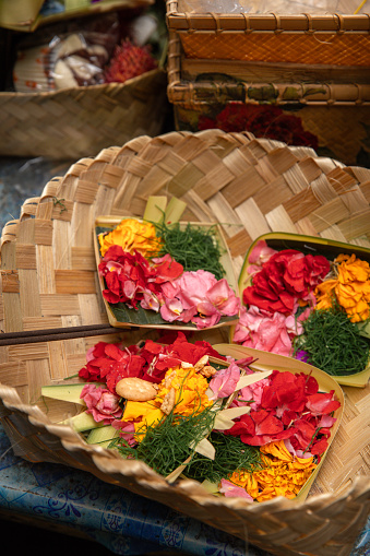 Religious offerings at Balinese shrine temple column with woven Bamboo basket full of flowers, fruit and incense stick