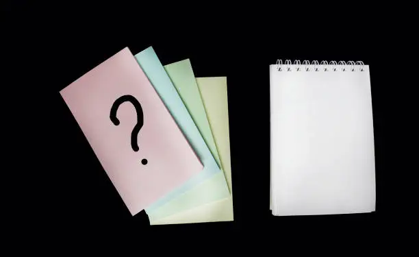 Question mark on a sticky note, next to a notepad for writing.Desk concepts for confusion, question or solution