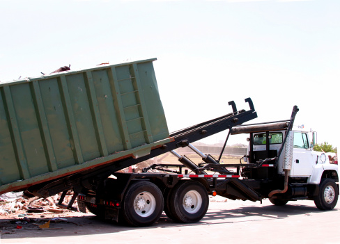 A dumpster loaded with trash is unloaded by a heavy-duty truck.