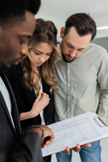 istock Smart, elegant African American woman with dark complexion carrying building papers while standing in front of a young couple with a family who are selecting a home for their family 1726481217
