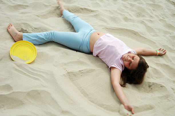 A young child sits next to a detailed sandcastle on the sandy shore, enjoying their creation
