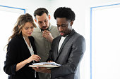 Young married couple reviewing the house plan with an African American real estate agent who is prepared to purchase a home in a new building with a blonde beautiful woman
