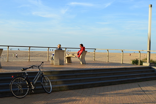 Ostend, West-Flanders, Belgium - October 1, 2023: caucasian couple sitting on a concrete designed outdoor park chair and admiring the beach scene in front of them