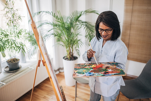 Mature black woman painting in living room at home.
