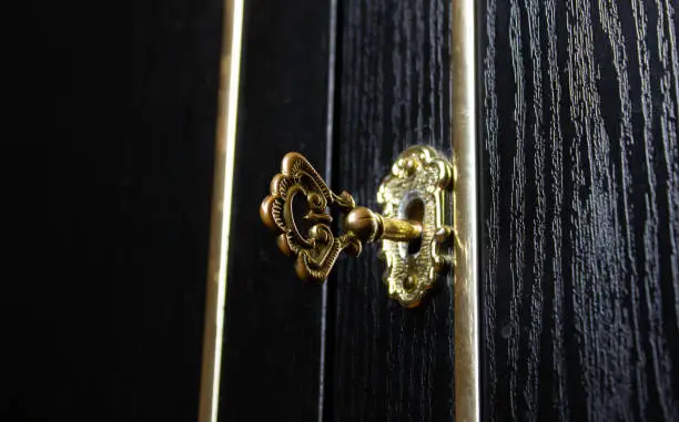 Key is in the keyhole of an antique cabinet door. Closed mysterious door with an old key.