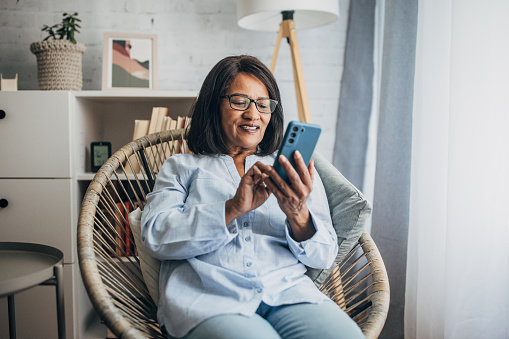 Mature black woman using smart phone while sitting in living room at home.