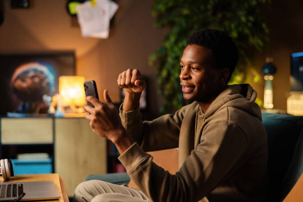 istock Attractive African American dark skinned social media content creator, using his phone to capture trendy videos and stay in touch with followers while editing content on his laptop 1726514434