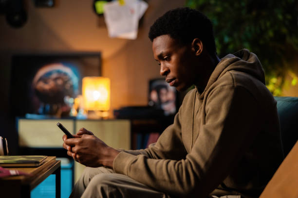 istock Concentrtated African American dark skinned musician, using his phone to record snippets of songs or jot down lyrics while mixing tracks on his laptop 1726514498