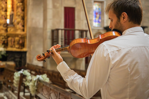 Person playing violin. Caucasian violinist man wearing classical clothes and performing in a closed space, church. Live performance. Horizontal image