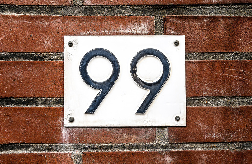 Address sign on residential building brick wall with number ninety nine. House identification signboard